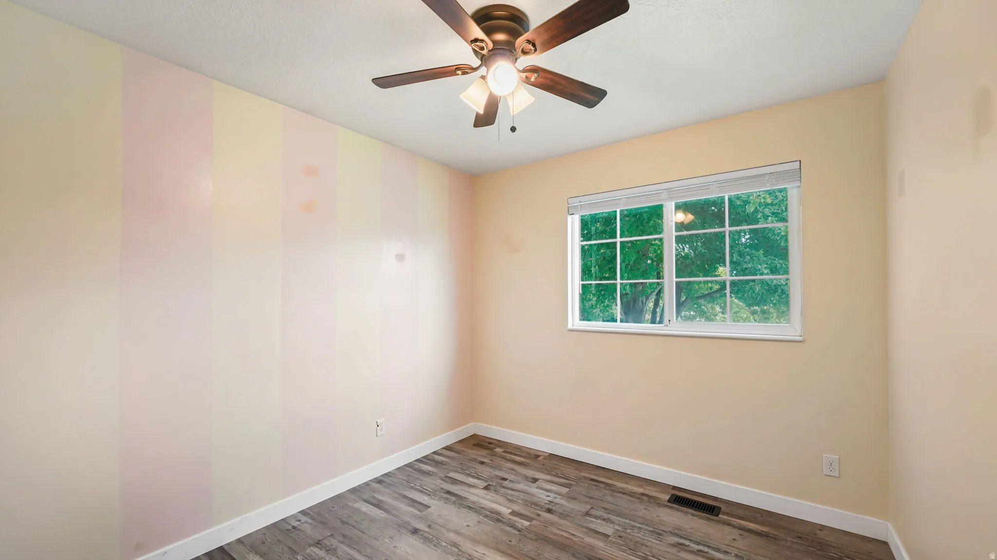 Wood-finish flooring, ceiling fan with light fixture, window with grid panes, and striped accent wall