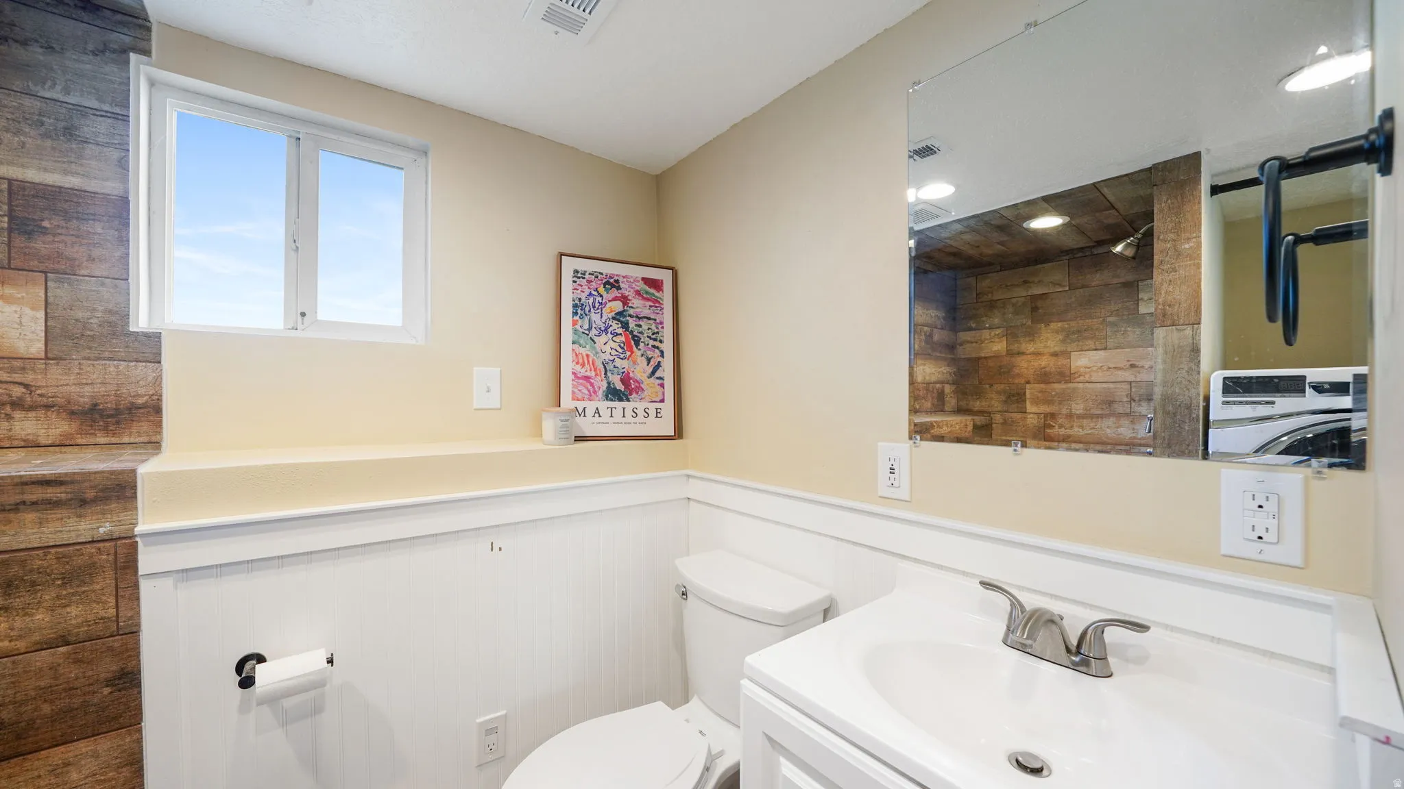 White vanity with integrated sink, rectangular wall-mounted mirror, and white wainscoting