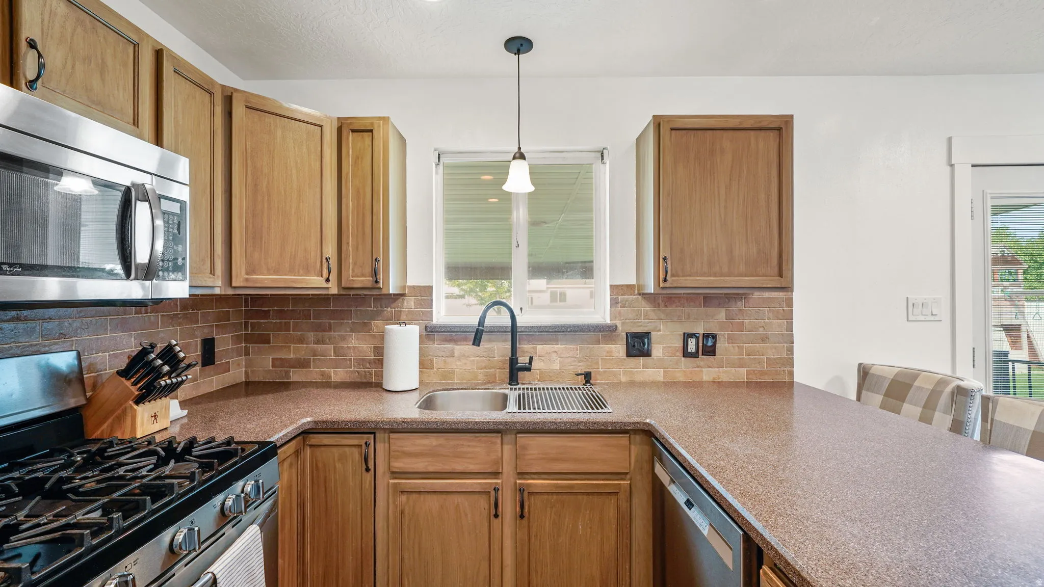 Kitchen featuring a stainless steel microwave, gas range, dishwasher, dual basin sink with a matte black faucet, and a tiled backsplash