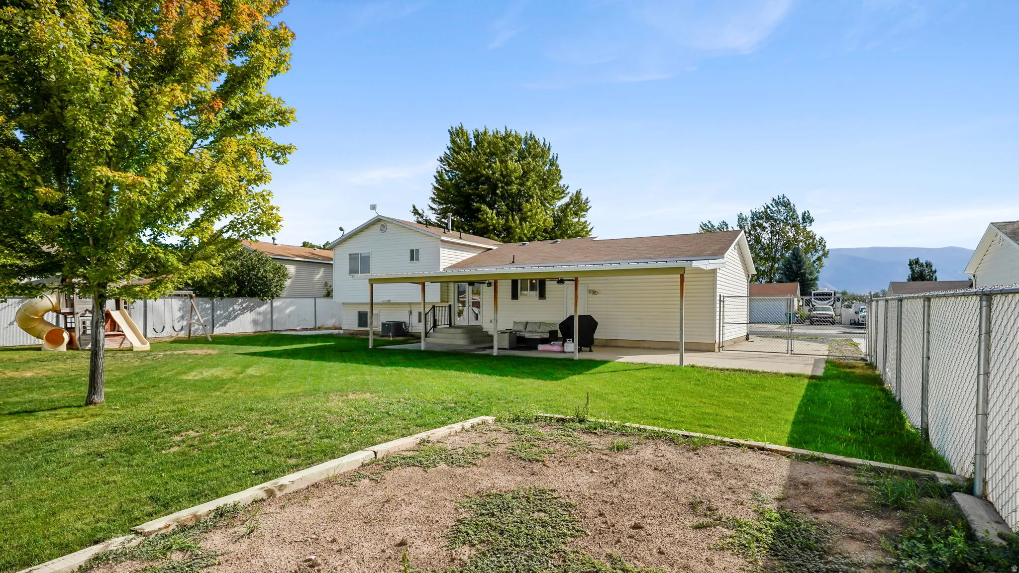 Expansive backyard featuring a covered patio, manicured lawn, and mature trees