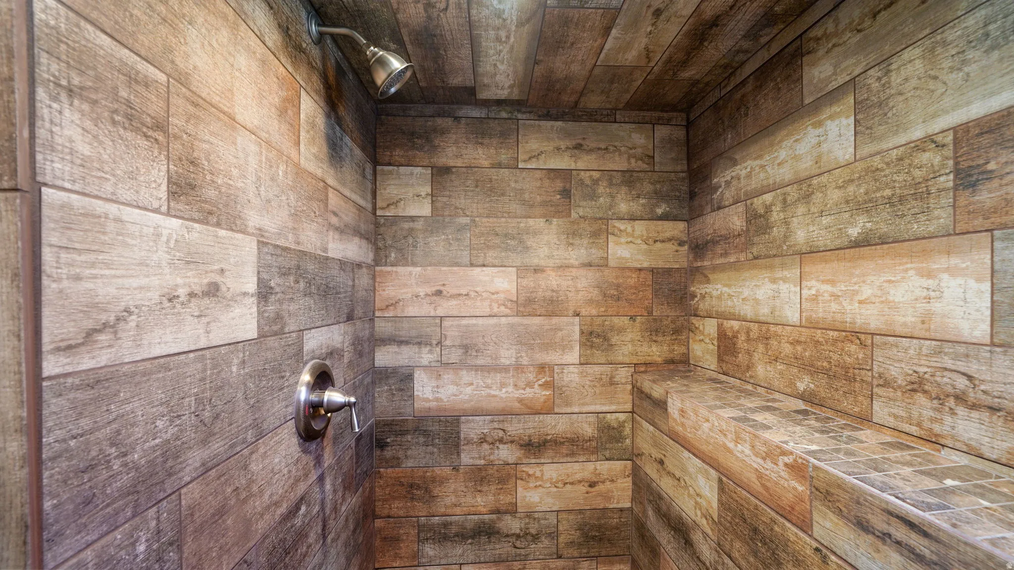Wood-look tile shower enclosure featuring a built-in bench, brushed nickel shower head, and coordinating control valve