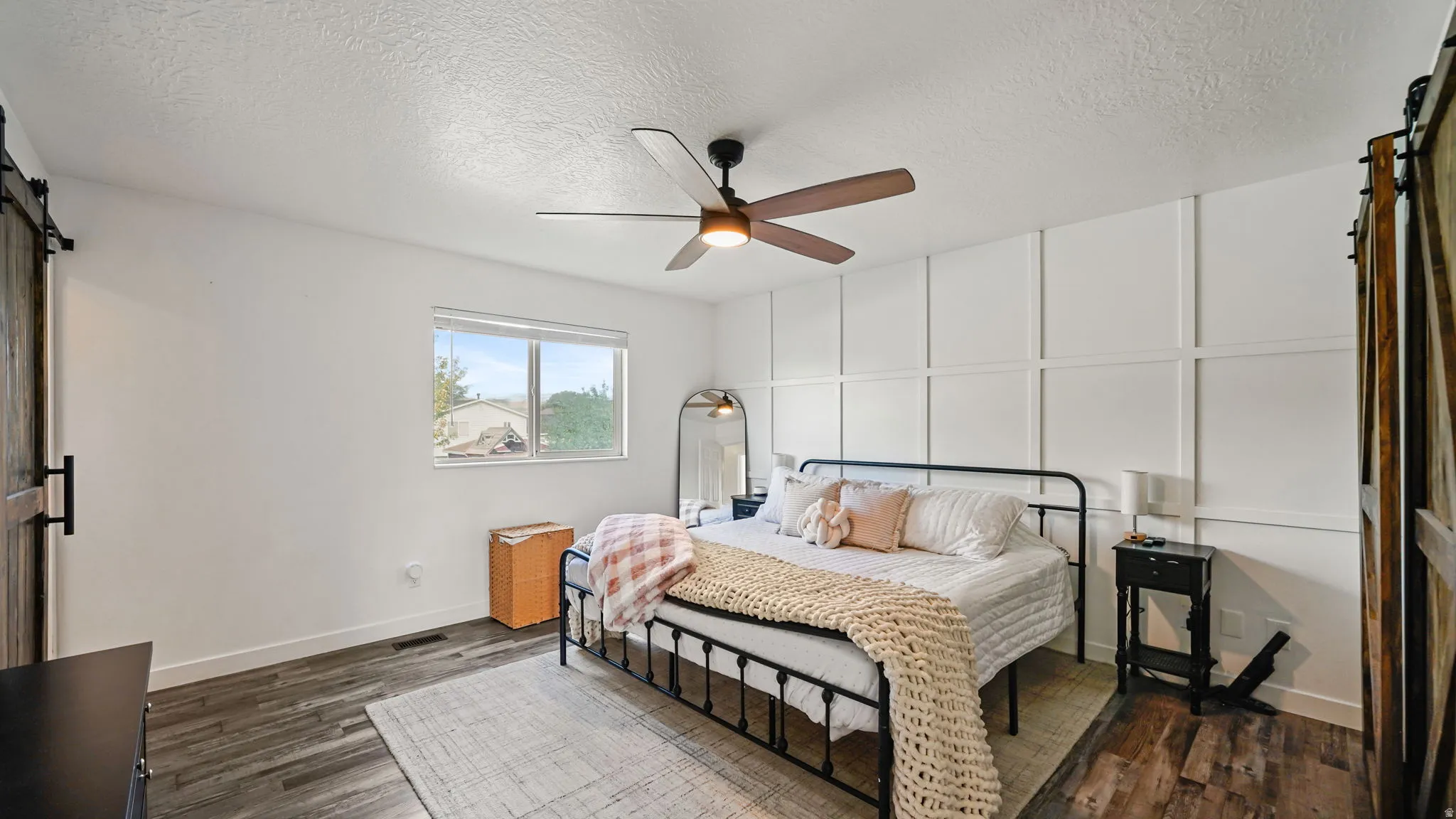 Wood-finish flooring, accent wall paneling, ceiling fan with light fixture, and a window providing natural light
