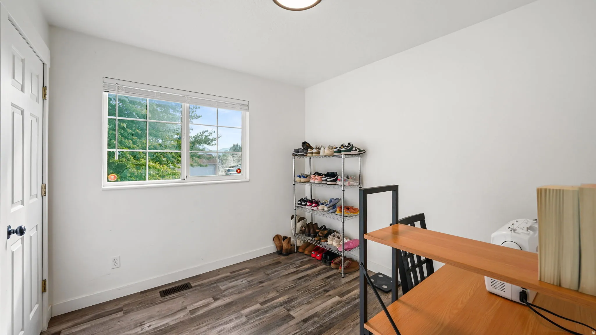 Wood-finish flooring, white paneled door with black hardware, and a window with blinds