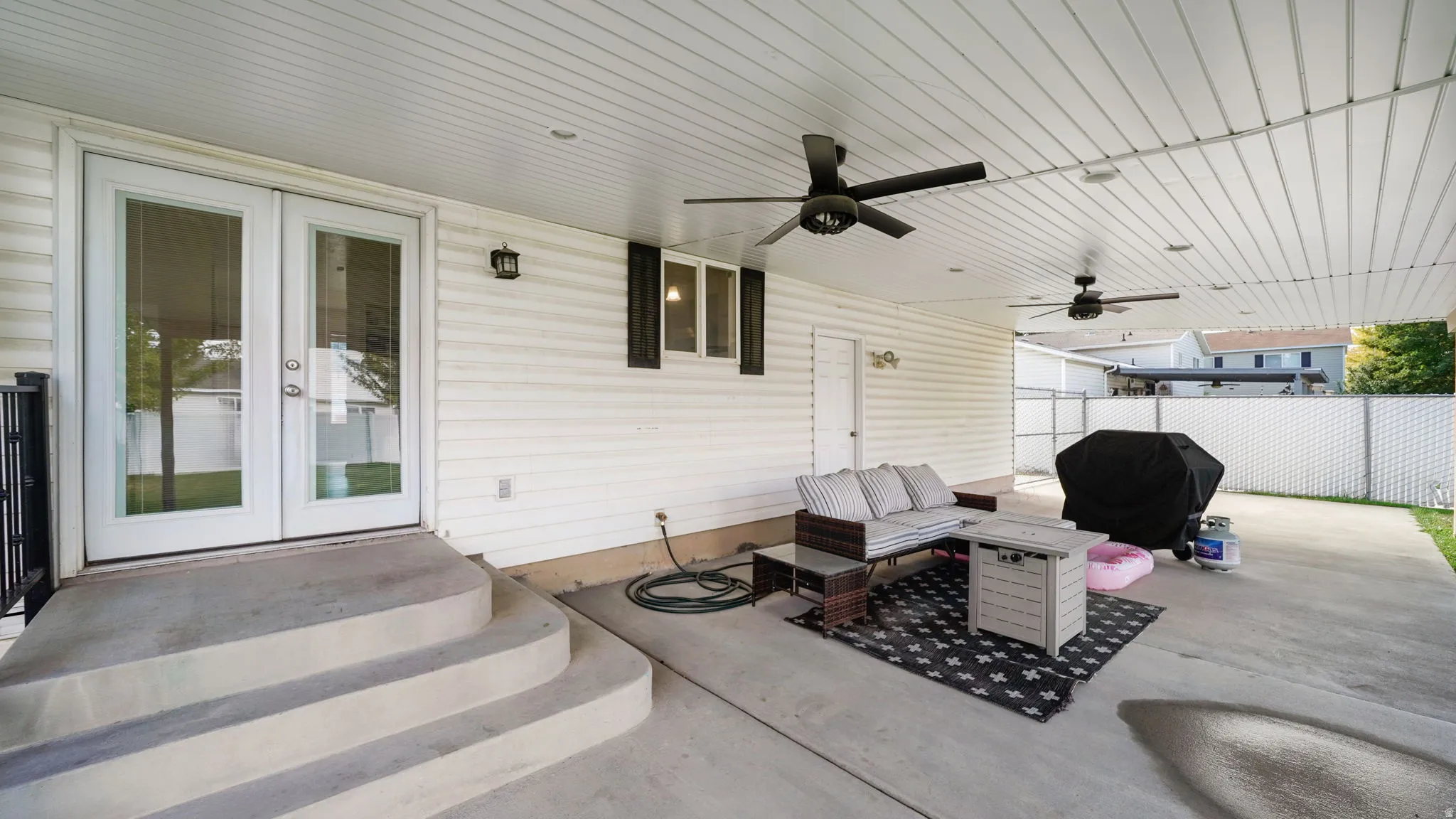 Covered patio with concrete steps, dual ceiling fans, and a white vinyl privacy fence