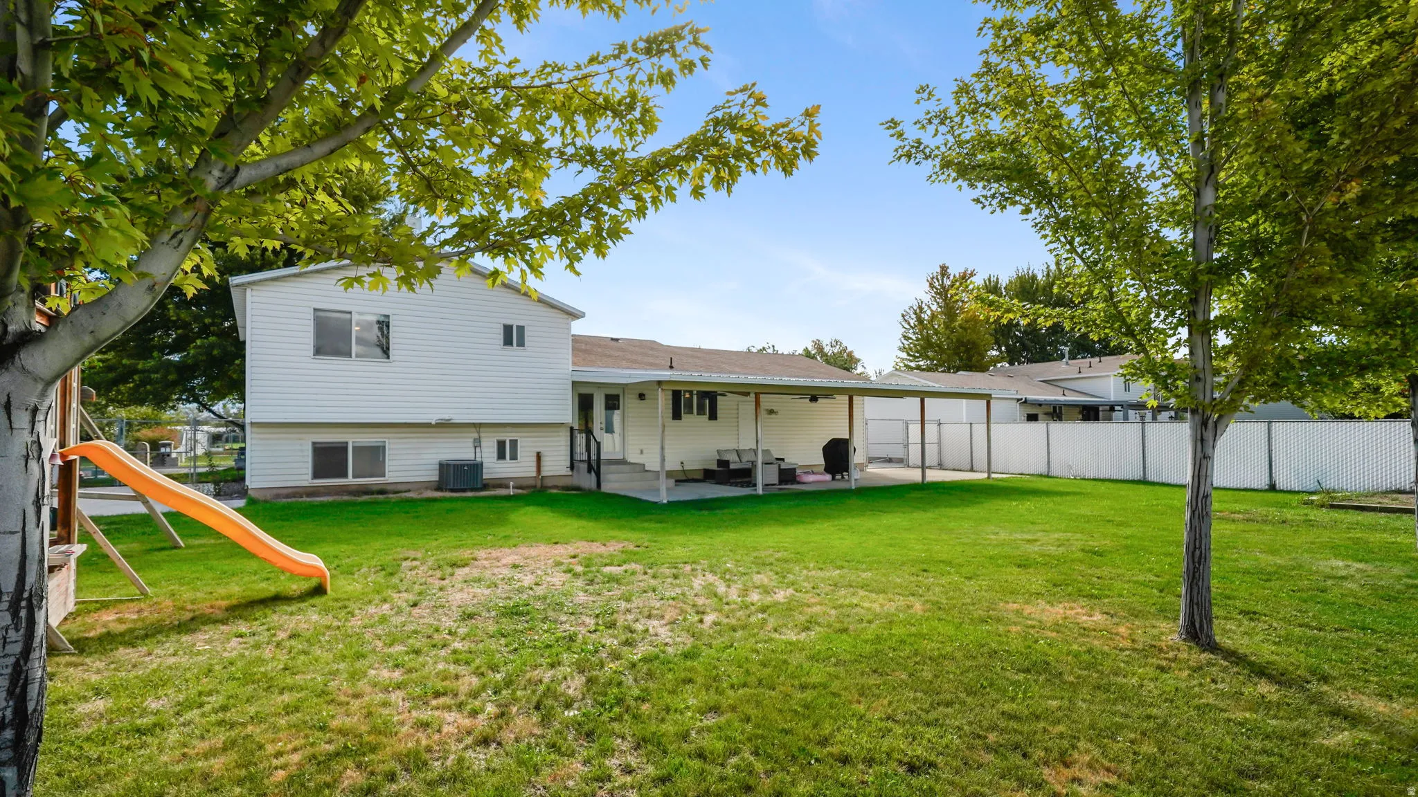 Expansive fenced backyard with a covered patio, a manicured lawn, and mature trees
