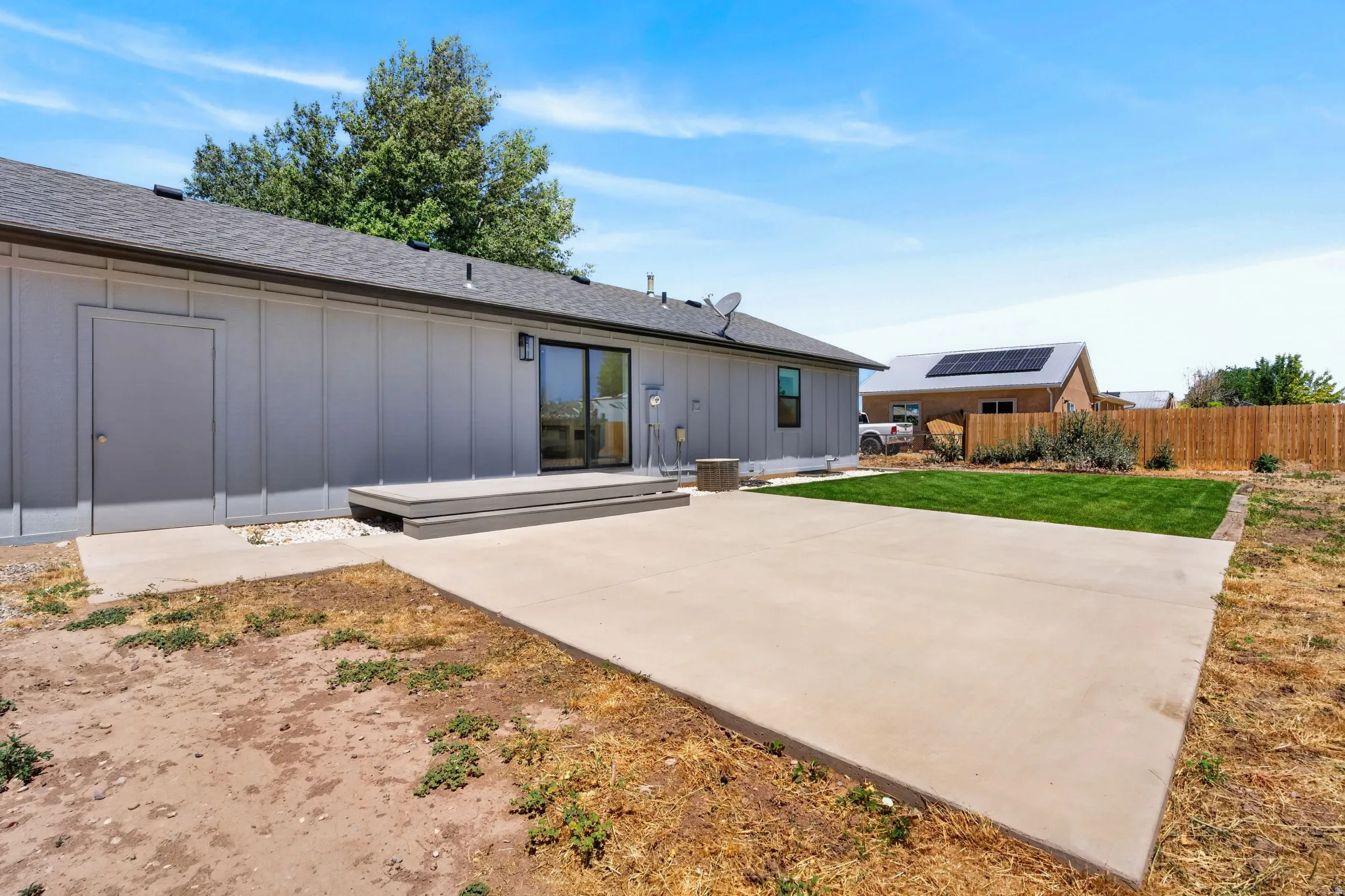 Expansive concrete patio, wood-finish deck, sliding glass door, manicured lawn, and wood privacy fence