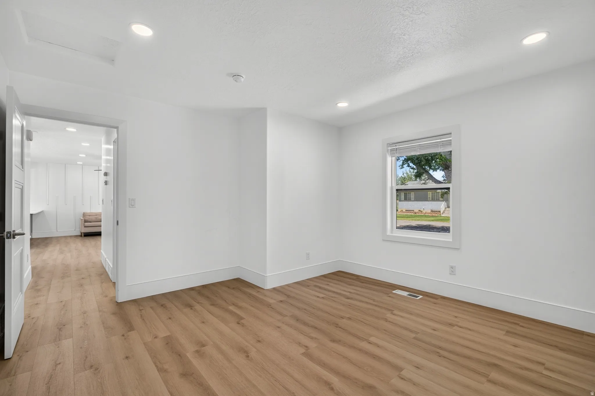 Recessed ceiling lighting, wood-finish flooring, white trim, white walls, and a window with a roller shade