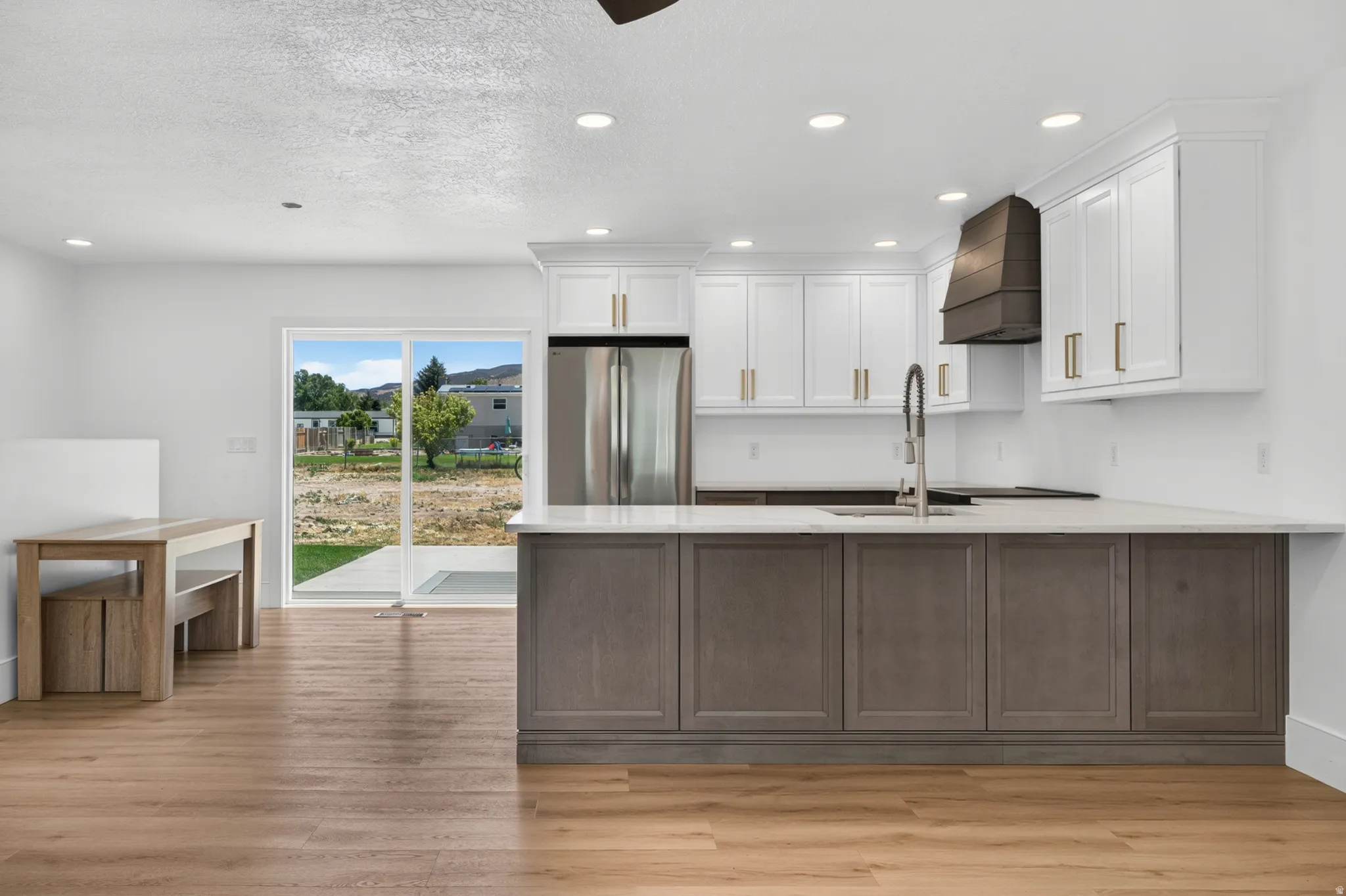 White upper cabinetry with gold-tone hardware, wood-finish flooring, stainless steel appliances, a kitchen island with gray lower cabinetry, and a sliding glass door