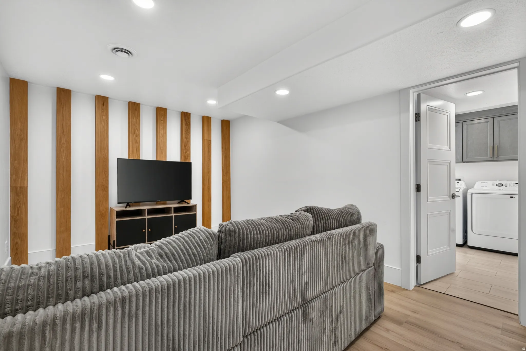Recessed ceiling lighting, wood-finish flooring, accent wall with vertical wood paneling, paneled door, and laundry area with cabinetry
