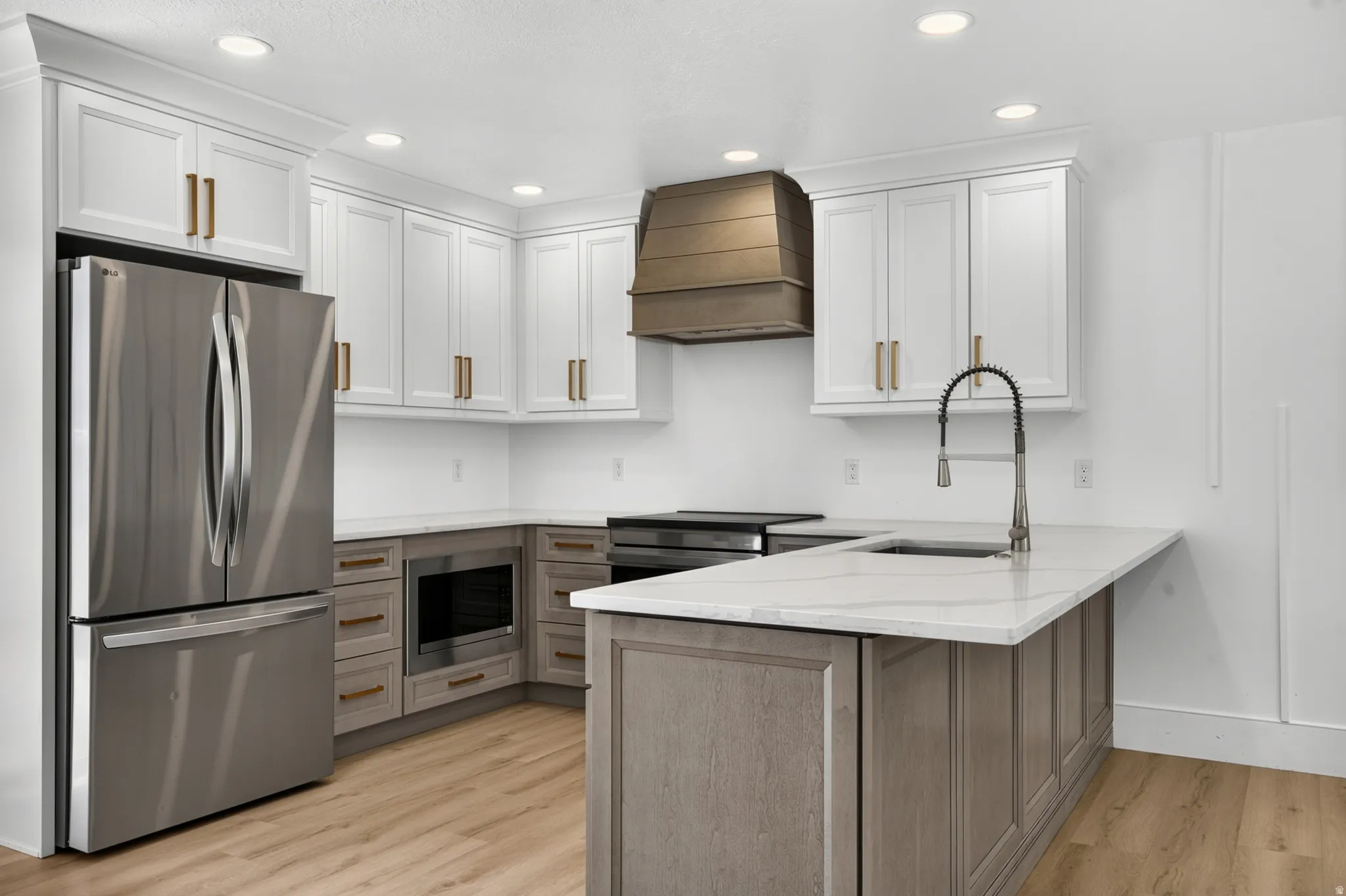 Kitchen featuring stainless steel appliances, white upper cabinetry, wood-finish lower cabinetry, a center island with sink, and light-tone wood-finish flooring