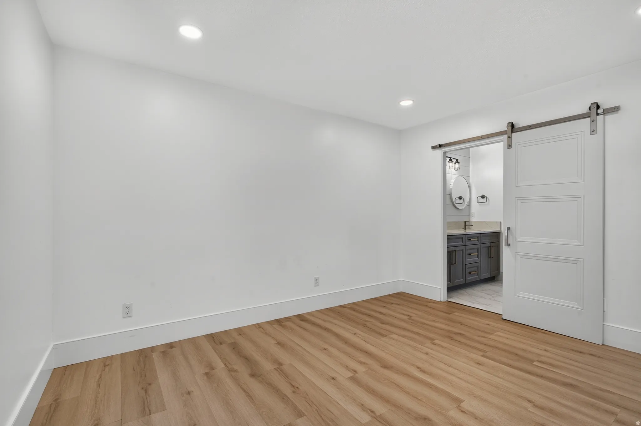 Recessed ceiling lighting, wood-finish flooring, white walls, and a sliding barn door entrance