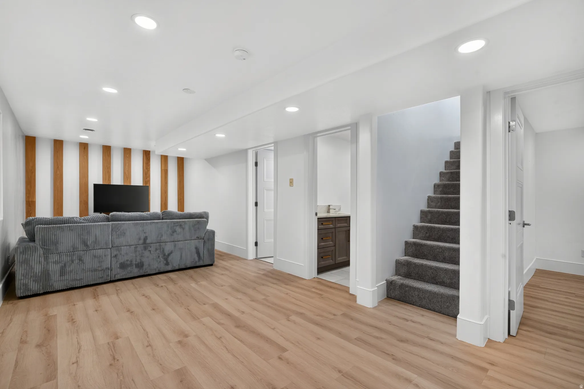 Wood-finish flooring throughout, recessed lighting, accent wall with vertical wood paneling, carpeted staircase, and built-in vanity with countertop