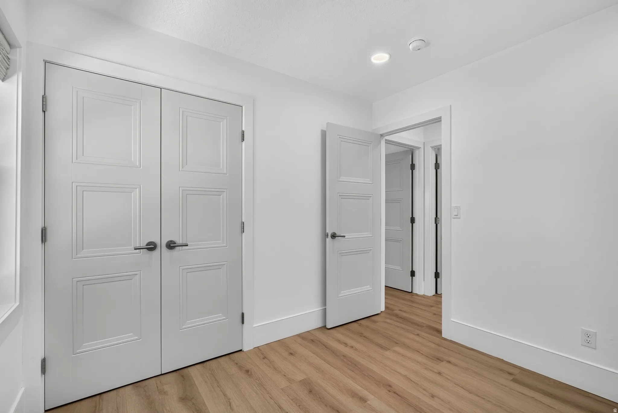Wood-finish flooring throughout, white walls, recessed ceiling lighting, and multiple paneled doors