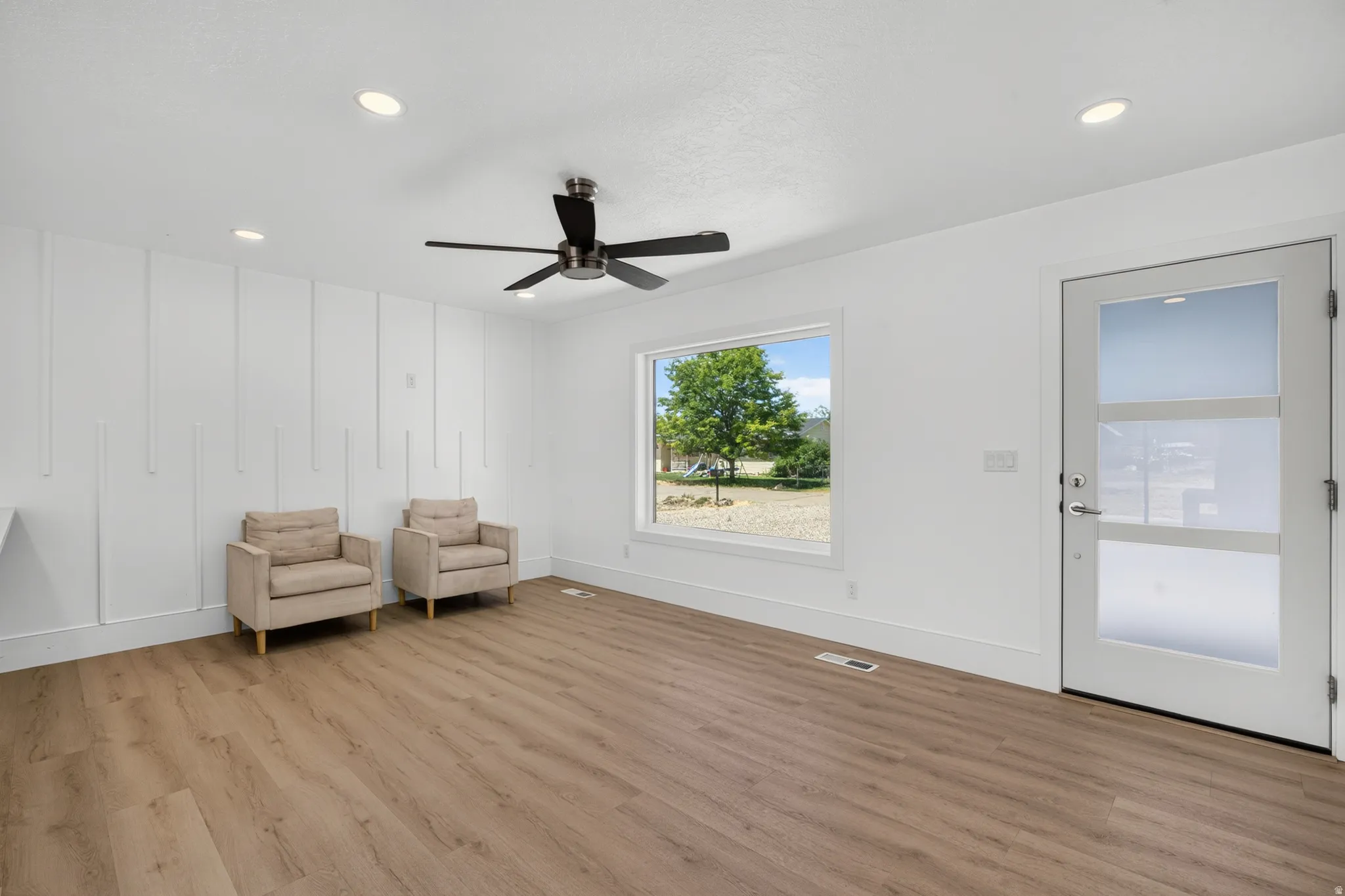 Wood-finish flooring with a modern ceiling fan, recessed lighting, and decorative wall paneling