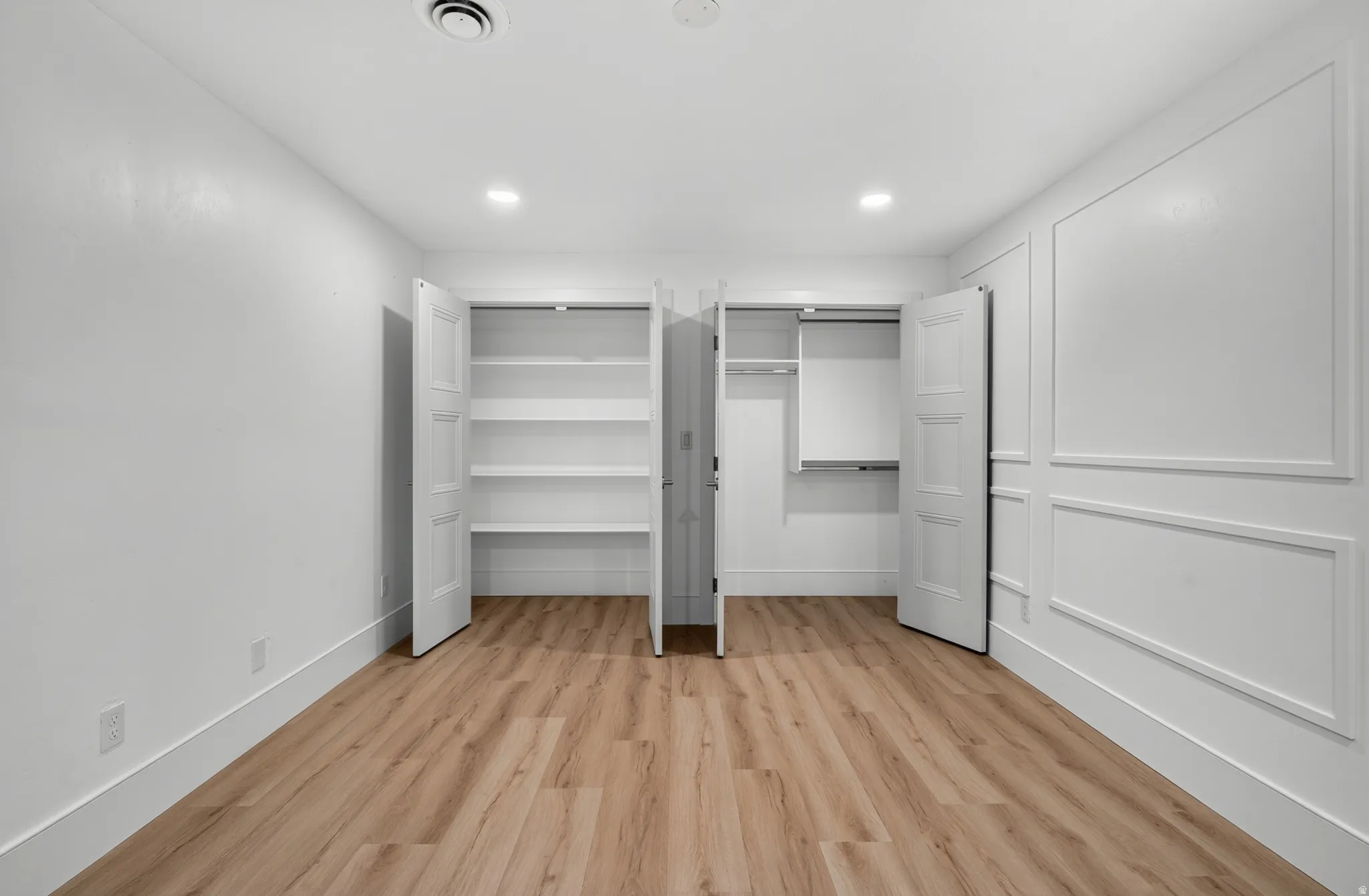 Wood-finish flooring, recessed lighting, and an accent wall with wainscoting details enhance this bright interior