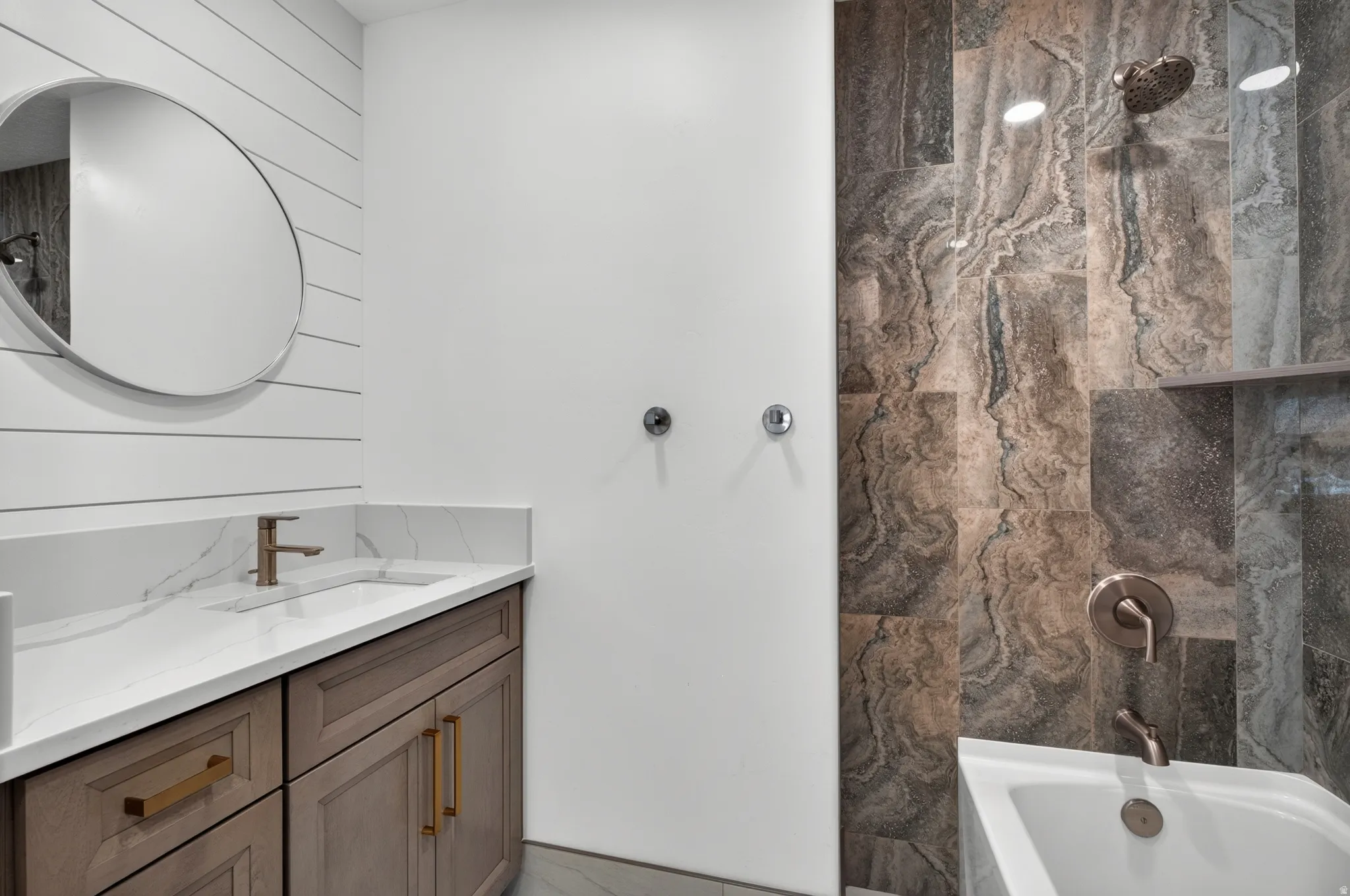 Modern bathroom featuring a wood-finish vanity with gold-tone pulls, a white countertop, and a circular mirror