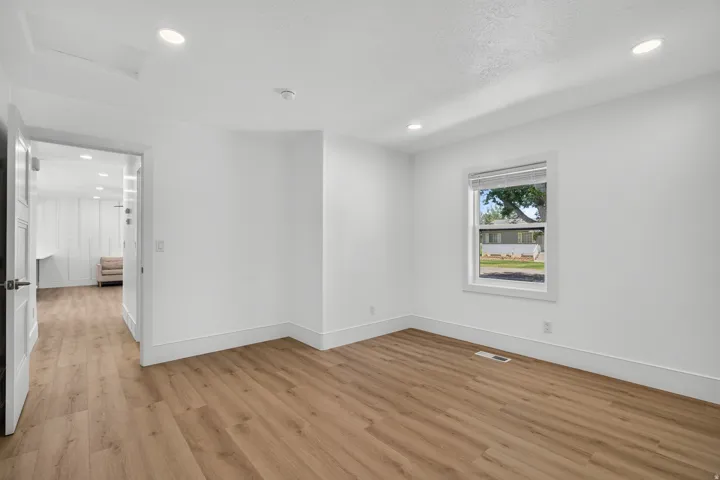 Recessed ceiling lighting, wood-finish flooring, white trim, white walls, and a window with a roller shade