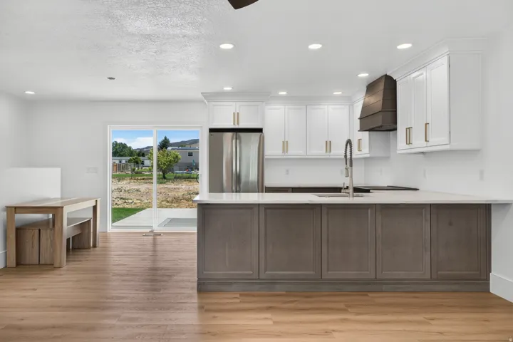 White upper cabinetry with gold-tone hardware, wood-finish flooring, stainless steel appliances, a kitchen island with gray lower cabinetry, and a sliding glass door