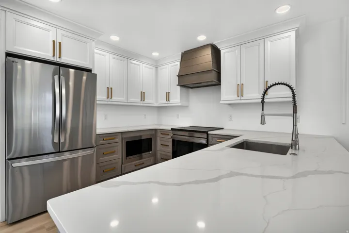 Stainless steel appliances, white shaker cabinetry, gold-finish hardware, quartz countertops, and a built-in microwave