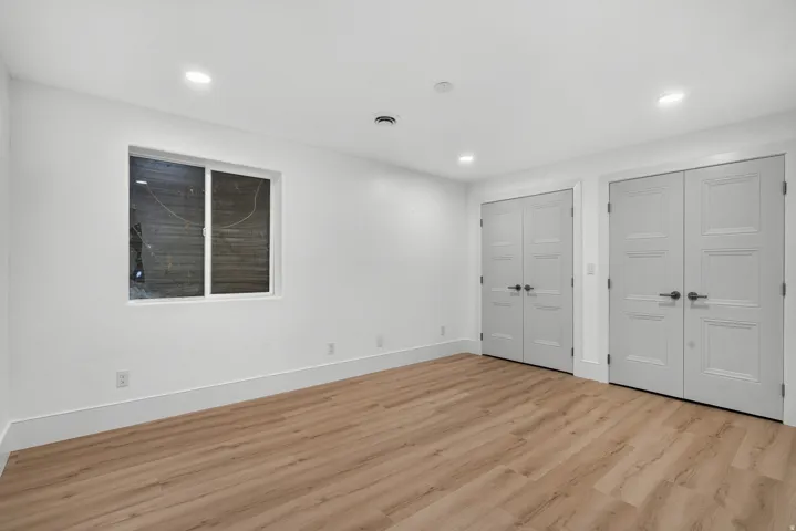 Wood-finish flooring with white walls, recessed lighting, white window frame, and two sets of double panel doors