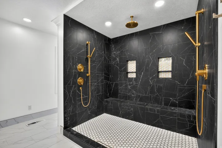 Spacious shower with black marble-finish tile, integrated bench seating, dual recessed niches, ceiling-mounted showerhead, and a handheld shower fixture