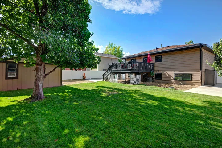 Expansive lawn featuring mature trees, a multi-level wood deck, a rear-entry garage, and a shed