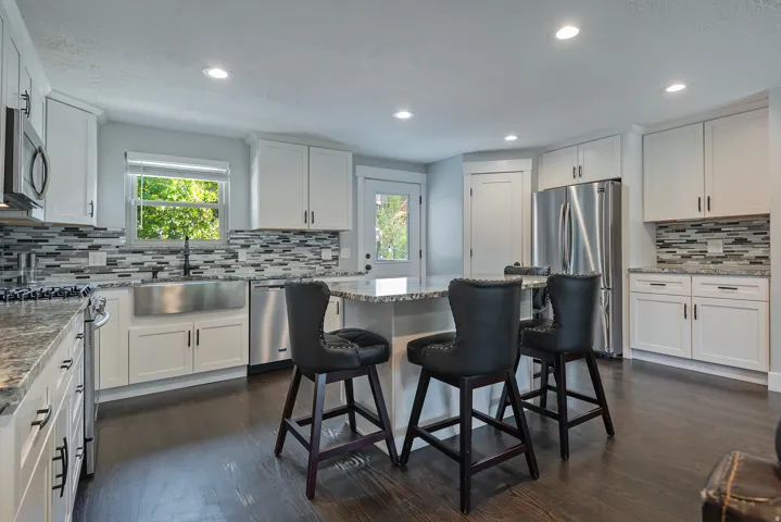 Kitchen featuring wood-finish flooring, white cabinetry, a stainless steel apron front sink, and a multi-tone tile backsplash