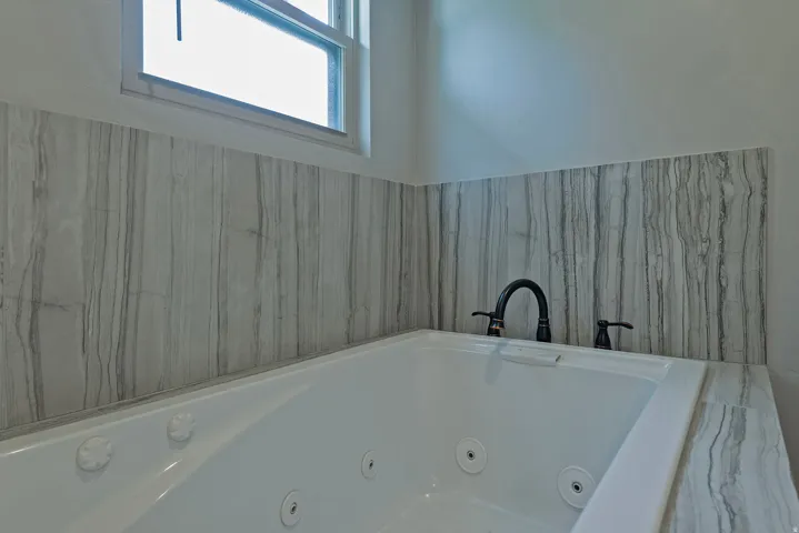 Jetted soaking tub with matte black fixtures, surrounded by vertically oriented striated wall tile, and a coordinating tiled tub deck