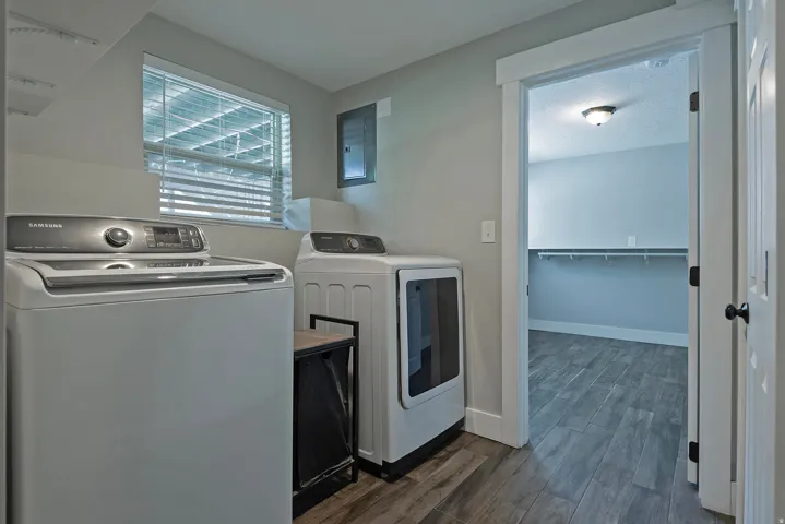 Laundry area featuring a window with blinds, wood-finish flooring, and built-in shelving in an adjacent space