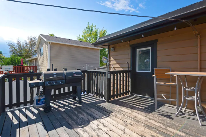 Wood-finish deck with a black railing, featuring a brown-sided exterior with a white-framed door