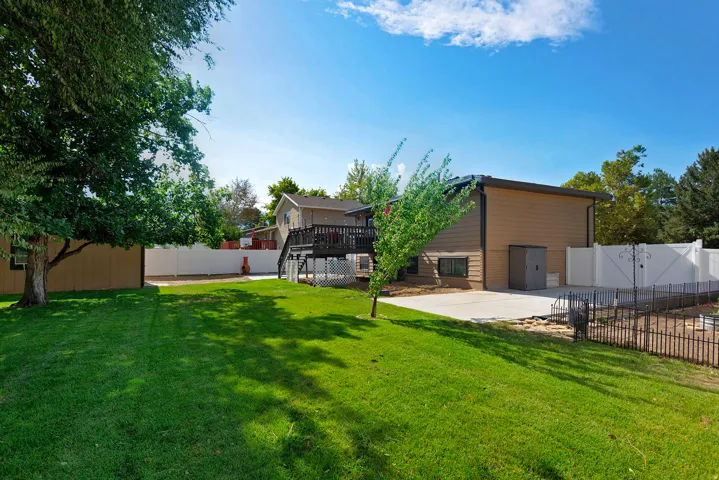 Expansive backyard with a manicured lawn, established shade trees, spacious concrete patio, multi-level wood deck, and white privacy fencing