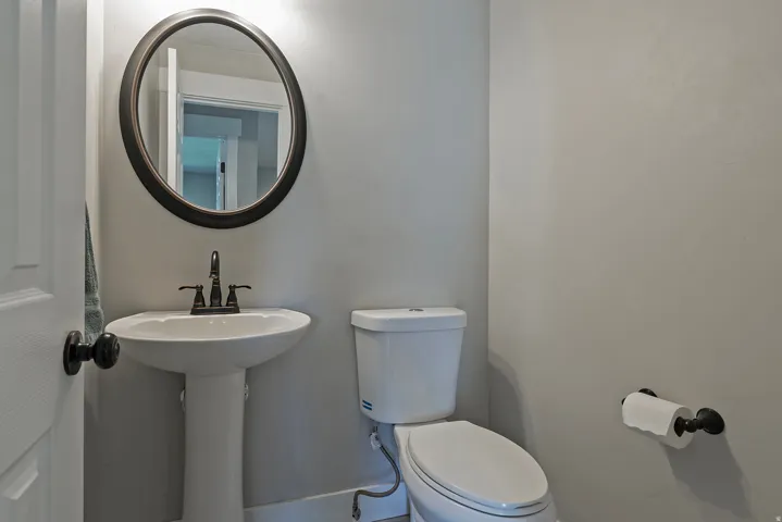 Pedestal sink with dark bronze faucet, oval mirror, and white toilet
