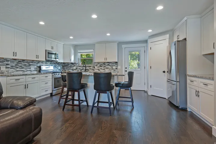 Recessed lighting illuminates the kitchen featuring white cabinetry, a tile backsplash, stainless steel appliances, and wood-finish flooring