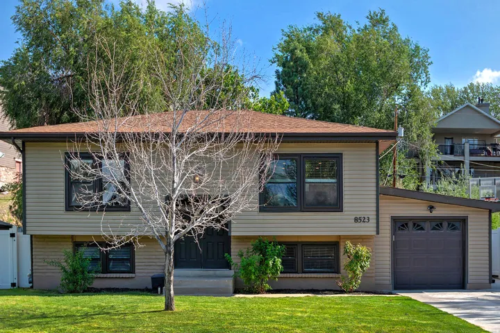Split-level residence featuring tan siding, a brown shingle roof, and dark-framed windows