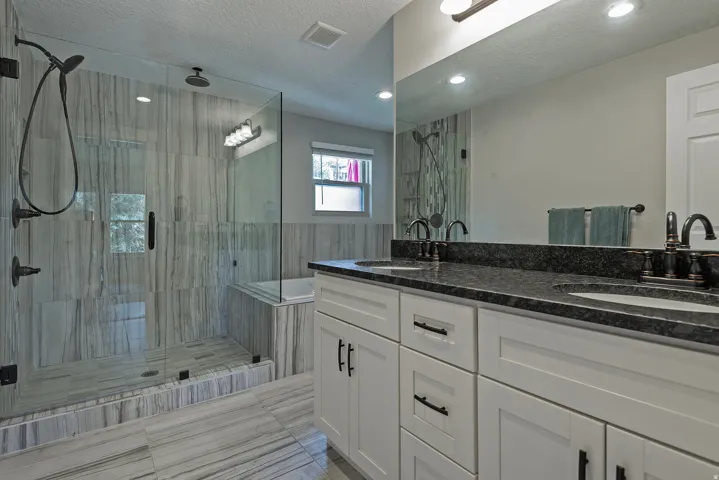 Dual vanity with dark stone-finish countertop, white cabinetry, and bronzed fixtures