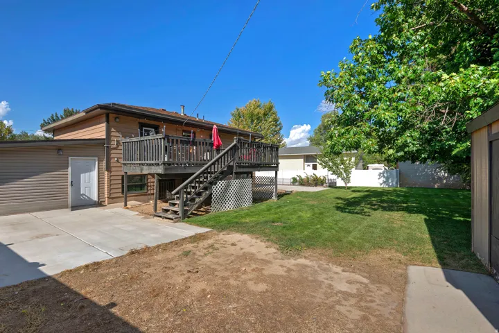 Rear exterior featuring a spacious wooden deck with railings, an expansive grassy yard, a concrete patio, and an attached storage shed