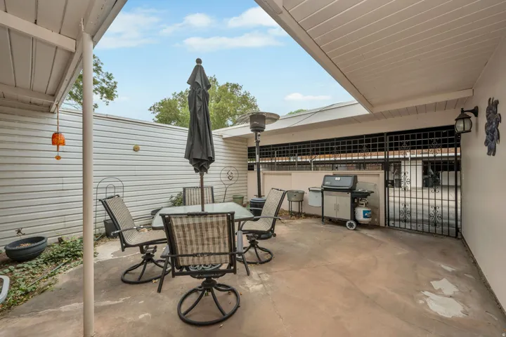 Covered patio with concrete flooring, wall-mounted exterior lighting, and a wrought iron gate