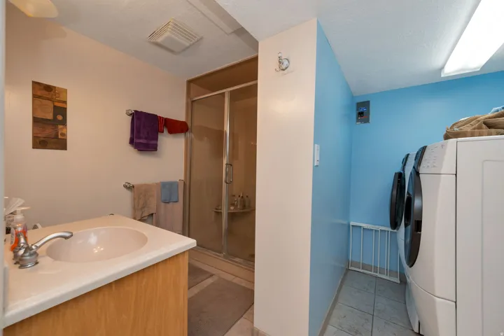 Vanity with integrated sink, glass-enclosed shower, tiled flooring, and laundry area with washer and dryer units