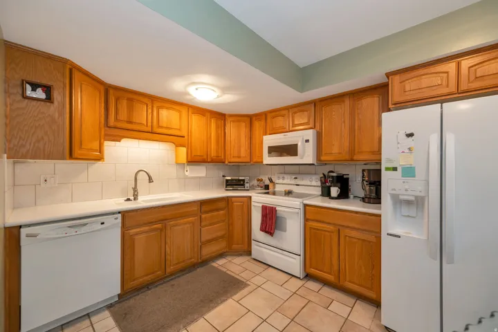Kitchen featuring wood cabinetry, white appliances, white subway tile backsplash, and tile flooring
