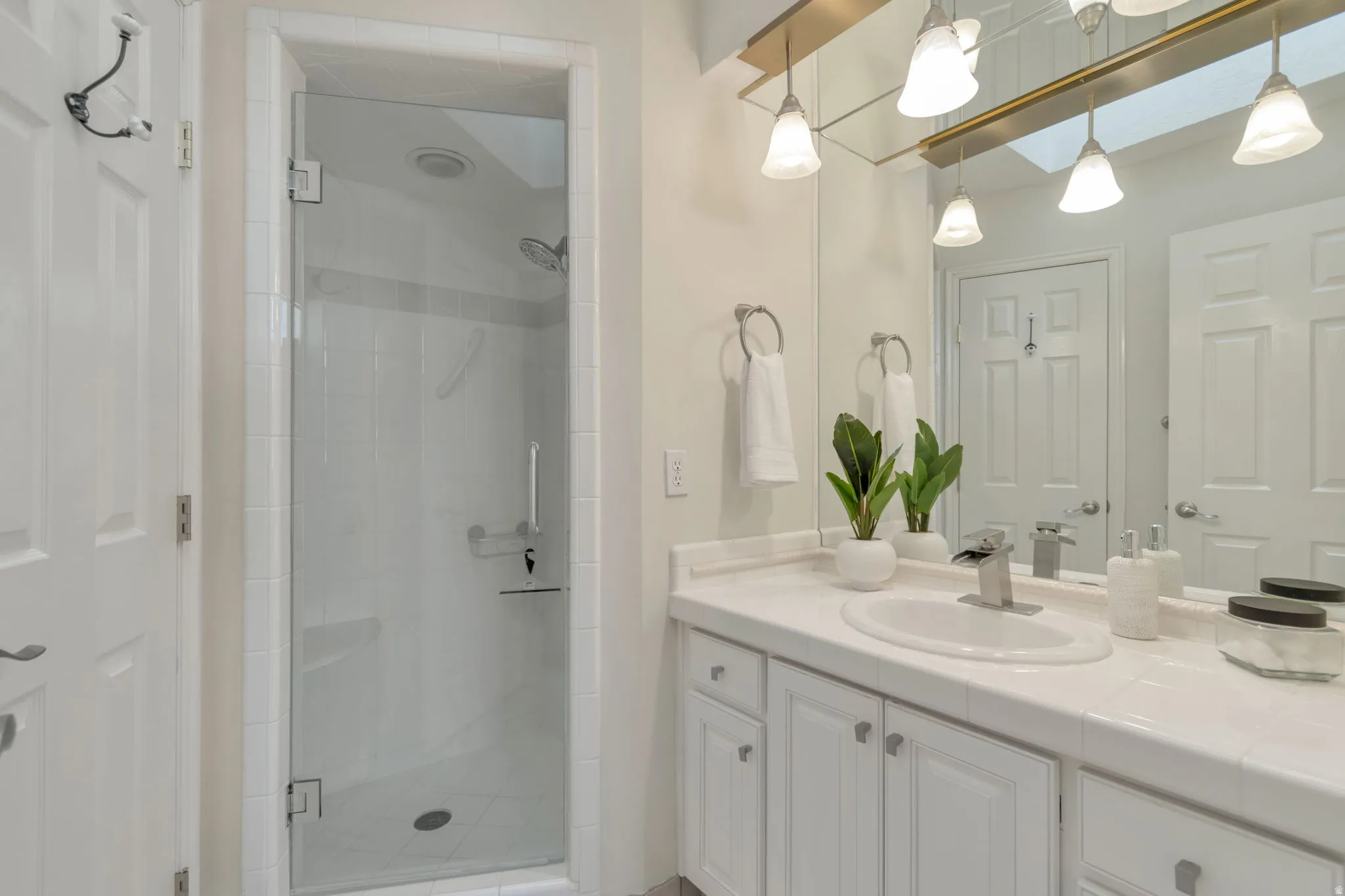 White vanity with integrated sink, brushed nickel faucet, large wall-mounted mirror, white shaker-style cabinetry, and glass-enclosed shower