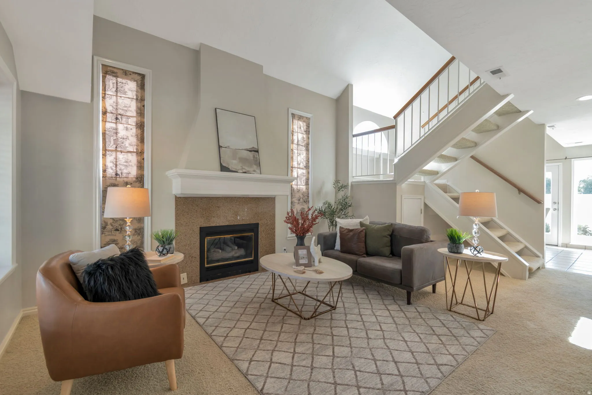 Fireplace with a stone surround and mantel, vaulted ceiling, staircase with white risers and wood handrails, tiled entryway, and wall-mounted windows