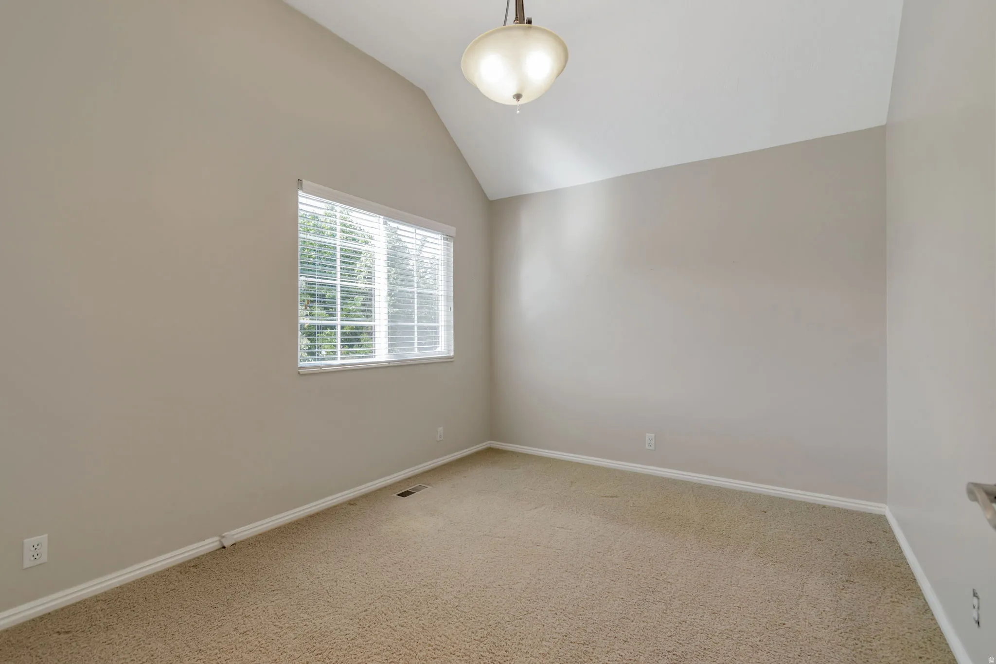 Vaulted ceiling, neutral wall paint, carpeted flooring, window with horizontal blinds, flush-mount lighting fixture