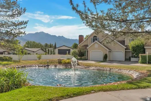 Lakeside property featuring a fountain, two-car garage, mountain backdrop, and light-toned exterior siding