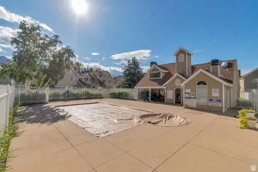 Outdoor swimming pool with a hardscape surround, white perimeter fencing, and a clubhouse with a covered patio