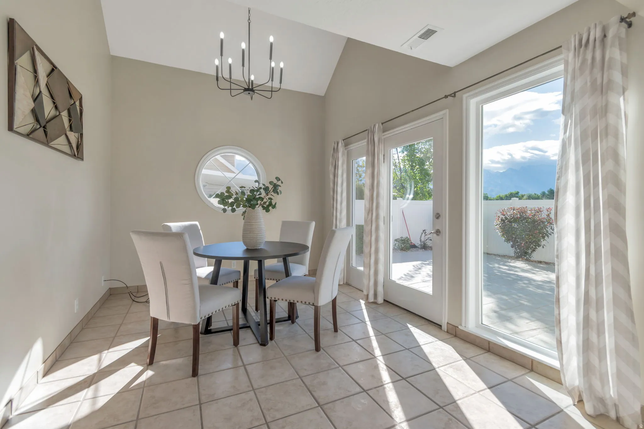 Vaulted ceiling with an angular design, black-finish chandelier, large glass pane door, additional large window, and tile flooring