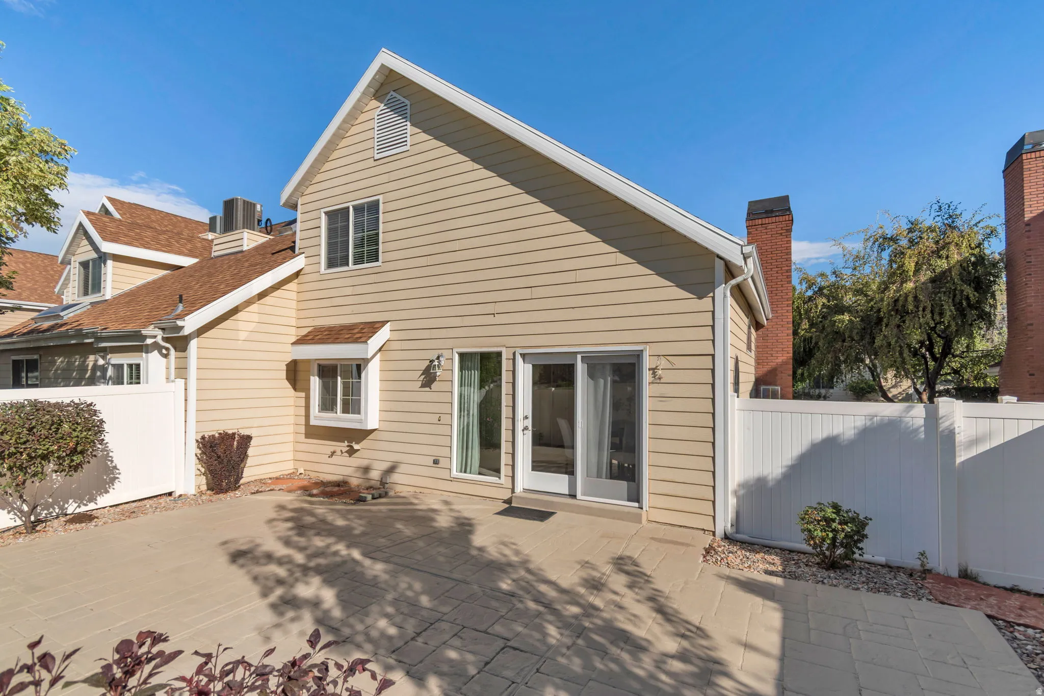 Paved patio area, siding exterior, dual-pane sliding glass door, white window frames, and private fencing