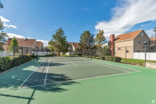 Green-surfaced tennis court with white line markings, surrounded by black chain-link fencing and mature landscaping