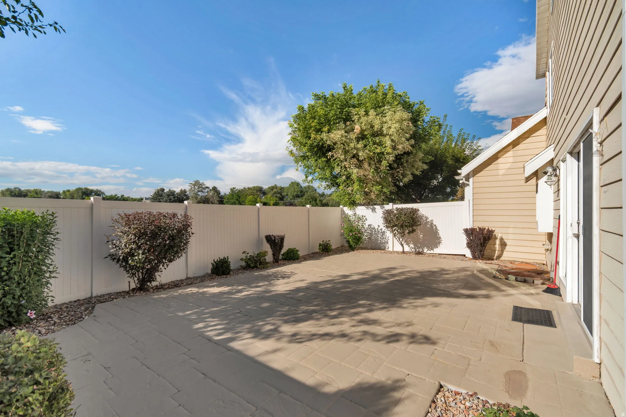 Paver patio with a white privacy fence, landscaping, and a siding exterior