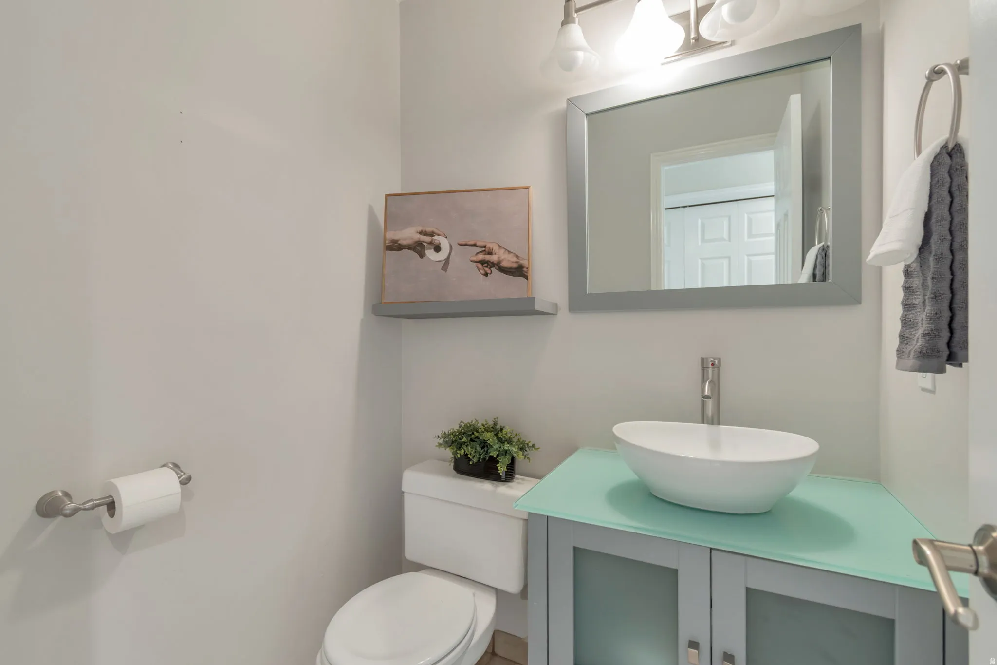 Powder room featuring a vessel sink, single-handle faucet, vanity with frosted glass cabinet doors, framed mirror, and wall-mounted light fixture