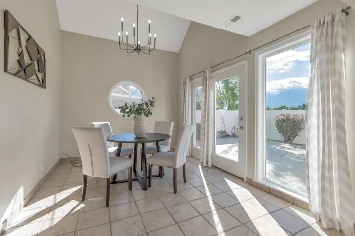 Vaulted ceiling with an angular design, black-finish chandelier, large glass pane door, additional large window, and tile flooring